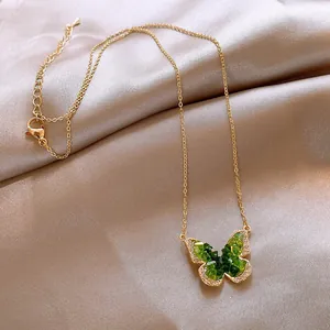 Close-up of a gold necklace featuring a sparkling green gradient butterfly pendant.