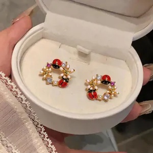 Dettaglio macro di orecchini a perno con coccinella e fiori placcati oro in scatola crema