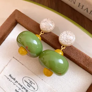 Close-up of green resin pendant earrings with textured cream top on a display board.