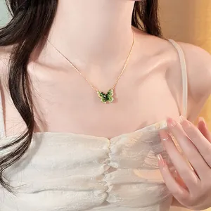 Close-up of elegant gold necklace with a green gradient butterfly pendant.