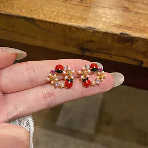 Vista dettagliata degli orecchini a ghirlanda di coccinelle e fiori placcati oro 18k.