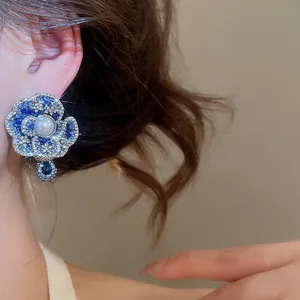 Close-up detail of blue flower stud earrings featuring rhinestones and a central pearl