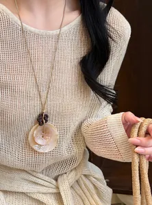 Close-up of retro resin disc necklace with leather cord on model wearing beige knitwear