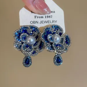 Detail view of retro blue rhinestone flower stud earrings with elegant pearl center.