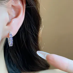 Detail view of a dainty silver hoop earring featuring purple zircons worn on a model's ear.