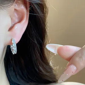Close-up of a sparkling silver hoop earring with multi-row pavé-set zircons on ear.