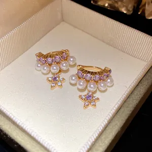 Gros plan de boucles d'oreilles dorées élégantes avec zircon, perles et pendentif étoile