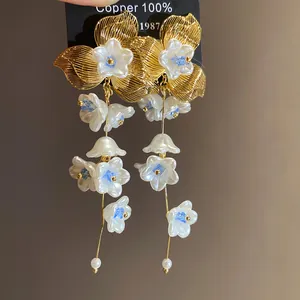 Detail view of golden floral tassel earrings with white pearls and blue crystals