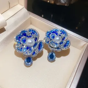 Macro view of blue crystal flower earrings with central pearl and teardrop charm