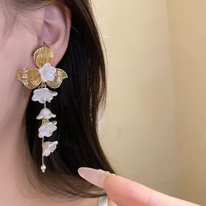 Detailed view of elegant white floral tassel earrings with gold leaf accents on ear