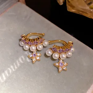 Gros plan sur d'élégants bijoux d'oreilles étoile dorée avec zircon violet et perles