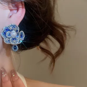 Detailed view of luxury blue and white rhinestone flower earring with central pearl.