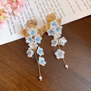 Close-up of white flower tassel earrings with gold leaf accents on a vintage paper background