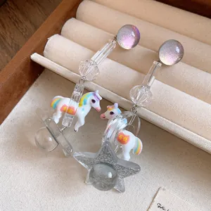 Close-up of resin unicorn and glitter star charms on silver pin drop earrings