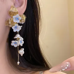 Close-up of vintage gold-tone flower tassel earrings with blue centers on an ear.