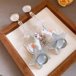 Close-up detail of whimsical resin unicorn and silver glitter star earrings in a jewelry box