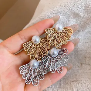 Elegantes pendientes de perlas con hojas huecas en oro y plata mostrados en mano