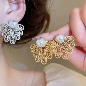 Primer plano de elegantes pendientes de perla con hojas caladas en oro y plata.