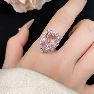 Close-up of a luxury pear-shaped pink zircon ring with a sparkling halo on a finger