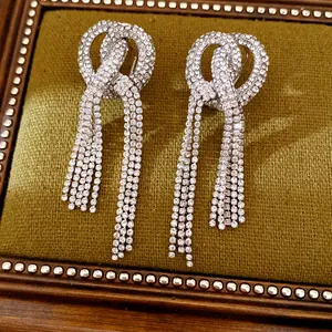 Close-up of sparkling rhinestone knotted tassel earrings on elegant green velvet background