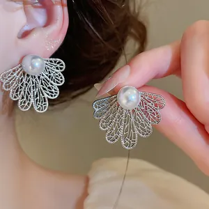 Primer plano de pendientes de hoja calada en plata con perlas blancas y texturas finas.