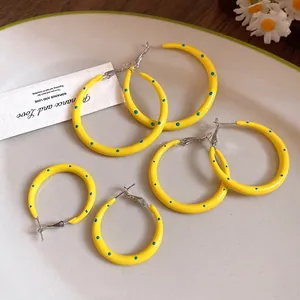 Pendientes de aro de esmalte amarillo con lunares en tres tamaños en un plato decorativo