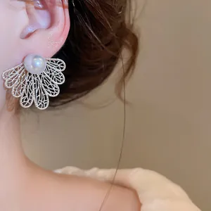 Primer plano de elegantes pendientes de perlas con hojas huecas usados por una modelo.