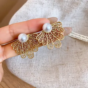 Detalle de pendientes de hoja calada dorada con una perla blanca central