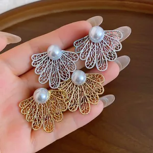 Vista detallada de elegantes pendientes de hoja hueca en oro y plata con perlas blancas.