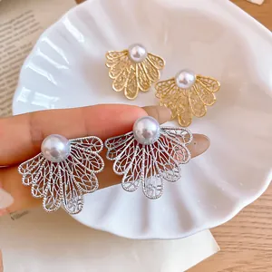 Primer plano de elegantes pendientes de perlas con diseño de hoja calada en metal.
