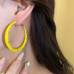 Detalle de un pendiente de aro amarillo con lunares azules usado por una modelo.