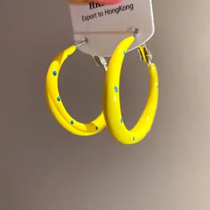 Detalle de pendientes de aro de esmalte amarillo con lunares azules y aguja de plata
