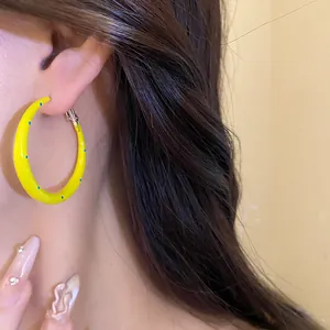 Primer plano de un pendiente de aro amarillo con lunares usado por una modelo.