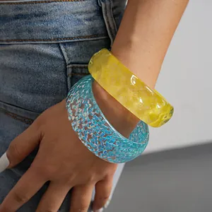 Close-up of colorful resin bangles in yellow and blue glitter on a model's arm.