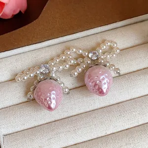 Close-up detail of sweet pearl bow earrings featuring dangling pink strawberry charms