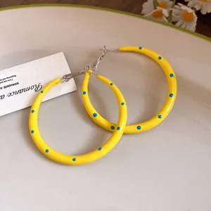 Primer plano de pendientes de aro amarillos con lunares azules y agujas de plata
