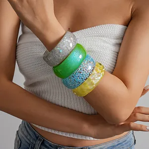Macro detail of four stacked colorful chunky glitter resin bangles on a model's forearm