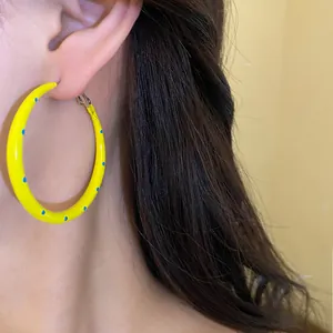 Detalle de cerca de aro de esmalte amarillo con lunares azules puesto en la oreja