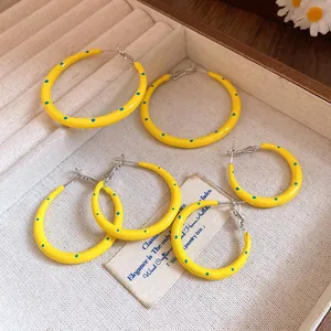 Vista detallada de vibrantes pendientes de aro en esmalte amarillo con lunares azules.