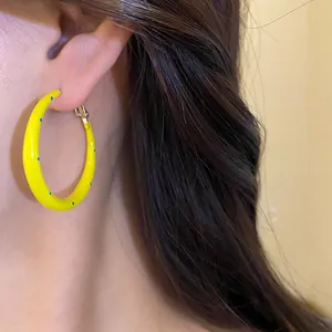 Primer plano de pendientes de aro de esmalte amarillo con diseño de lunares azules