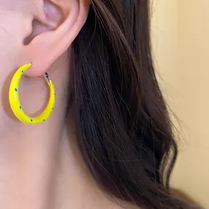 Detalle de un pendiente de aro amarillo con lunares azules en la oreja de una modelo real