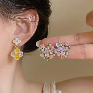 Detailed macro view showing sparkling zircon floral earrings and a clover drop earring on ear.