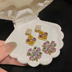 Detailed close-up view of zircon flower and clover earrings presented in a shell jewelry box.