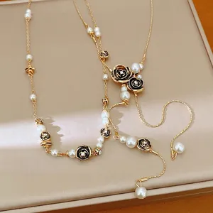 Elegant gold-tone necklace featuring white pearls and black rhinestone rose charms on tray