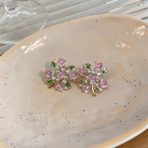 Detailed macro view of pink and green zircon flower stud earrings with gold finish