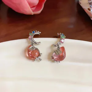 Macro view of dainty silver earrings with colorful crystals and pink strawberry pendants