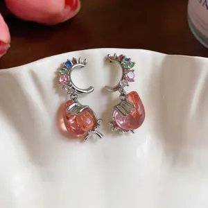 Detail shot of French style earrings with zircon crescents and pink resin strawberries.