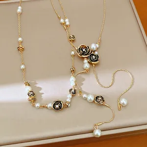 Detail shot showing the elegant pearl and black rose charms on a gold chain necklace.