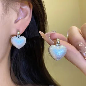 Close-up of heart-shaped earrings with iridescent pearlescent finish and silver hoop