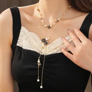 Close-up of a layered gold necklace featuring black flower charms and white pearls on a model